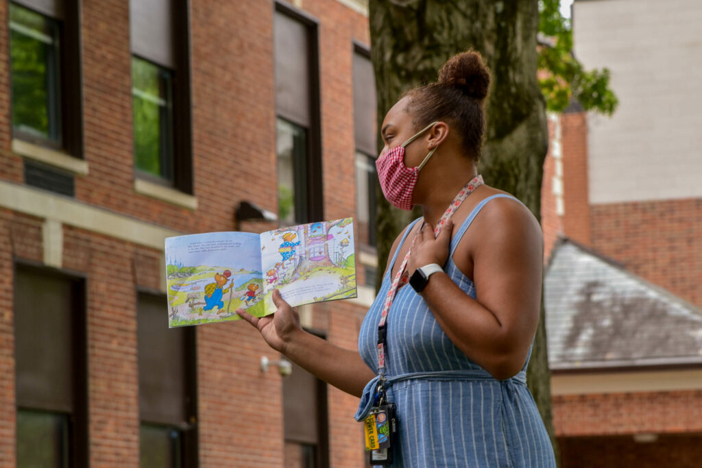 Black teacher wearing face mask reads a book outside