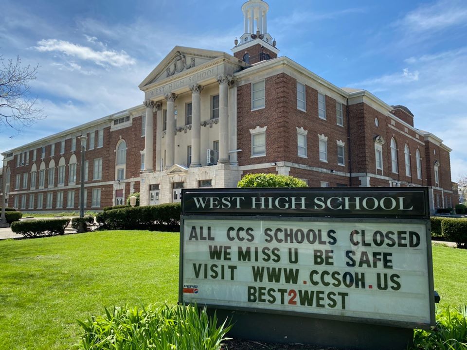 Exterior of a high school and sign that says "All CCS schools closed. We miss U. Be safe"