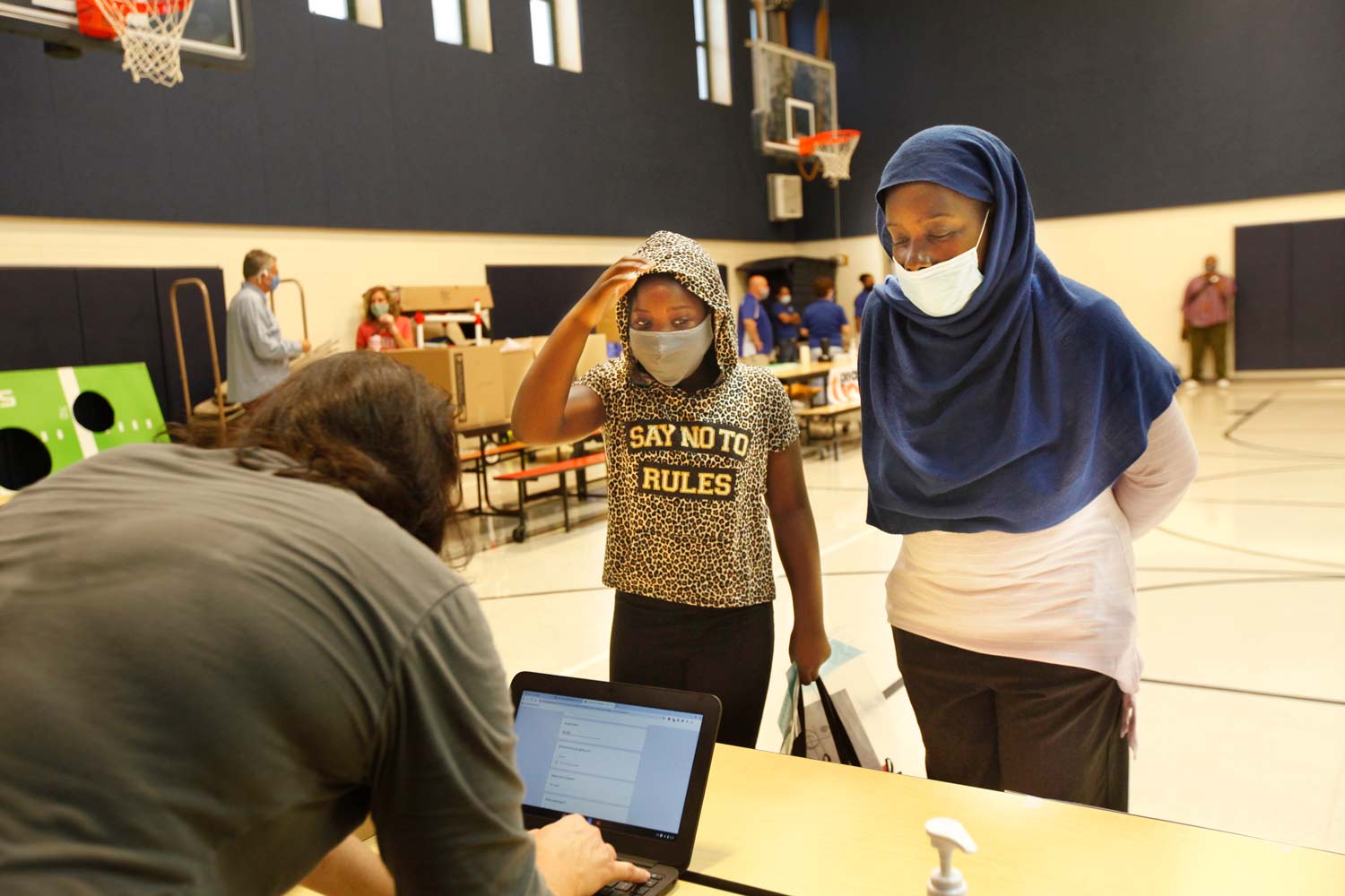A girl and her mom, who is wearing a hijab, check in with school staff to get school supplies