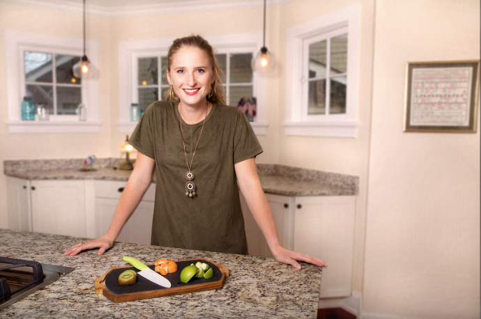 Elizabeth Biel stands behind a kitchen island with a cutting board of fruit in front of her