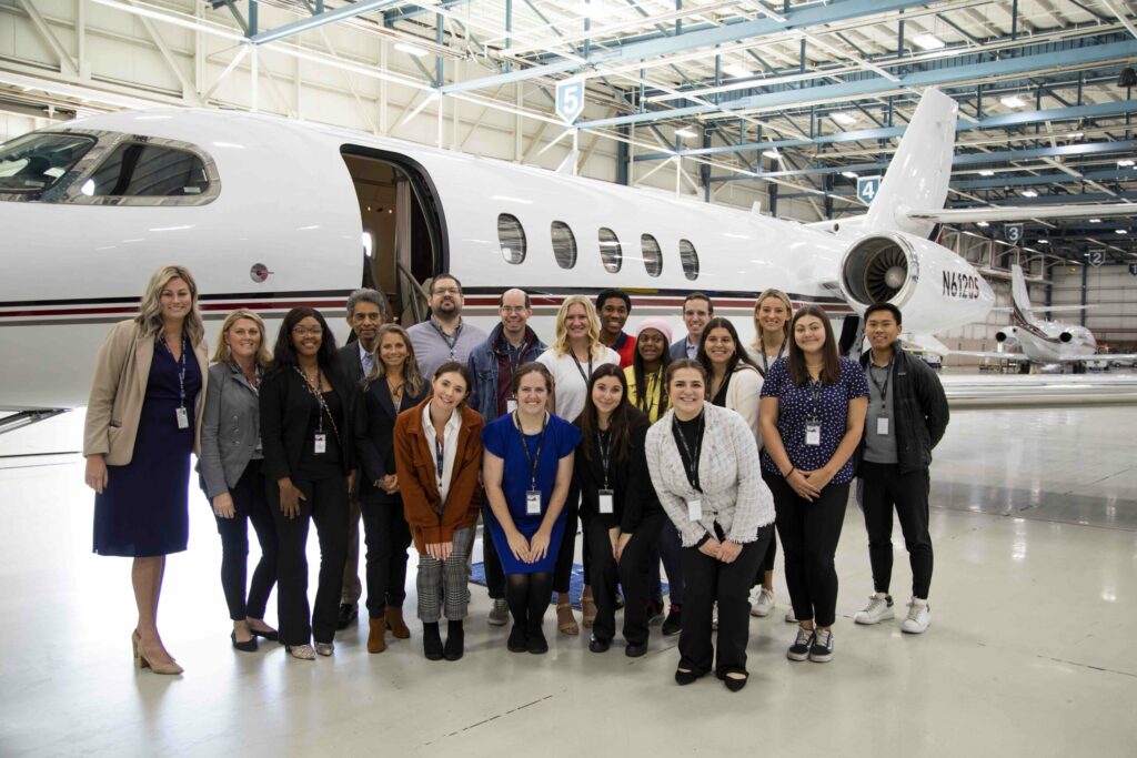 Ohio State students posing for photo in NetJet hanger next to airplane