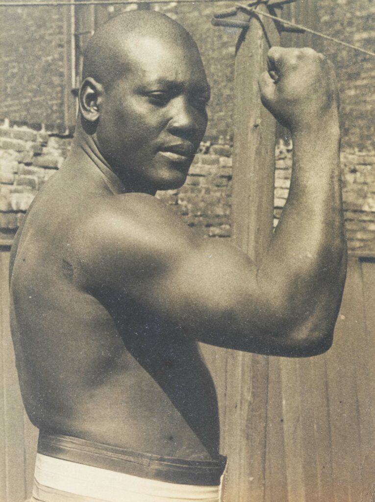 Boxer Jack Johnson in black and white photo flexing
