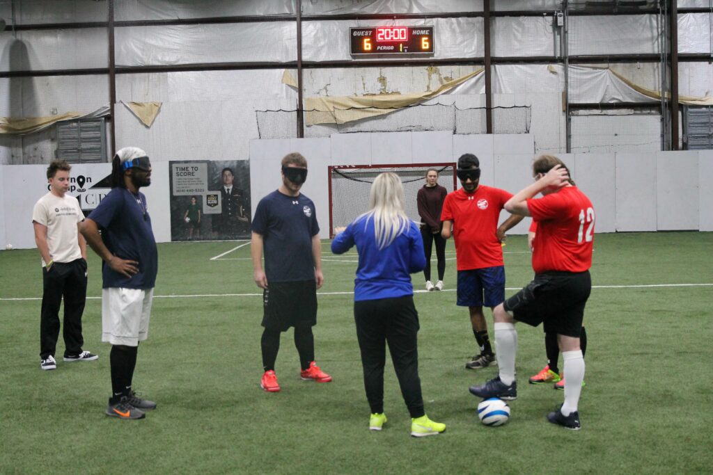 Katie Smith coaching blind soccer players on indoor pitch.