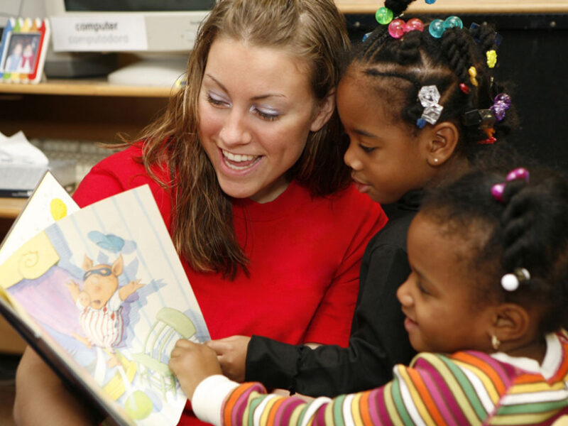 Teacher reading a picture book to two young students