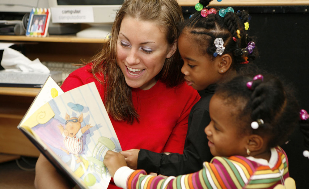 Teacher reading a picture book to two young students