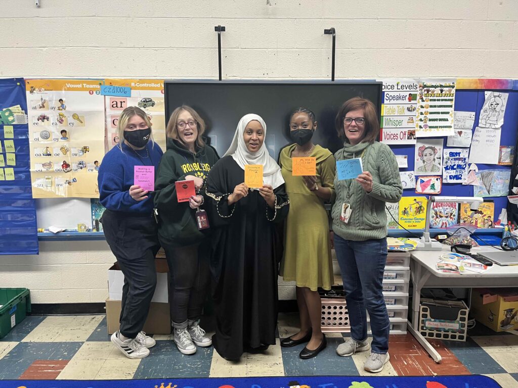 Teachers posing in the front of an elementary school classroom each holding a different KEEP BOOK