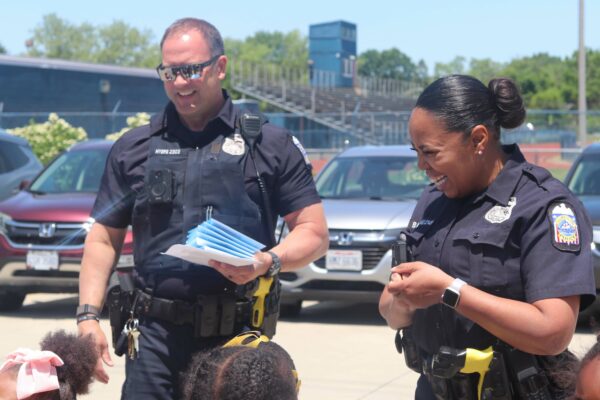 Police officers talking to a group of school age children in a parking lot on a sunny day
