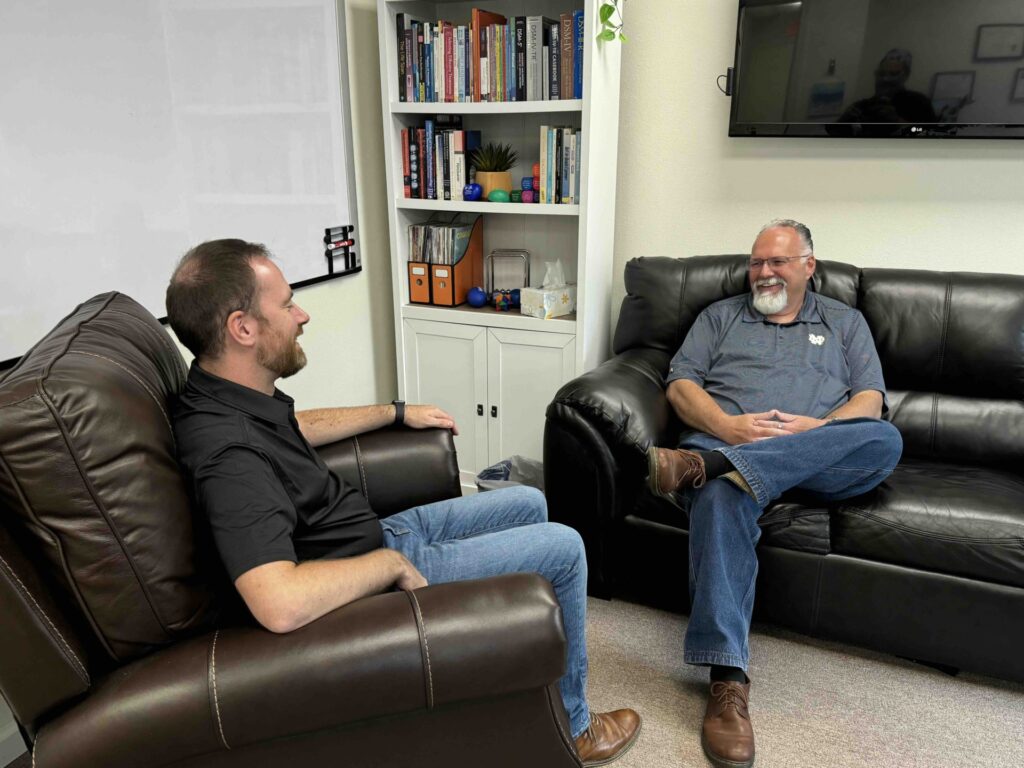 Derek Lee sits on a couch talking to a colleague