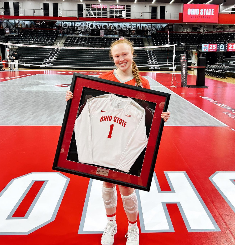 Sarah Morbitzer holding her framed jersey on the Ohio State volleyball court