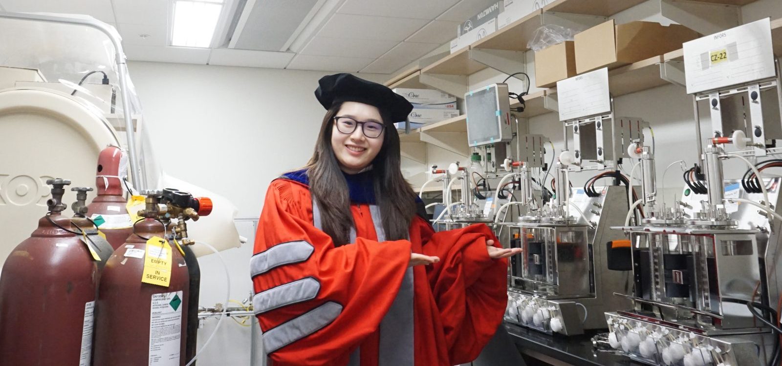 Shiqi Zhang in graduate regalia showing off the equipment in the lab.